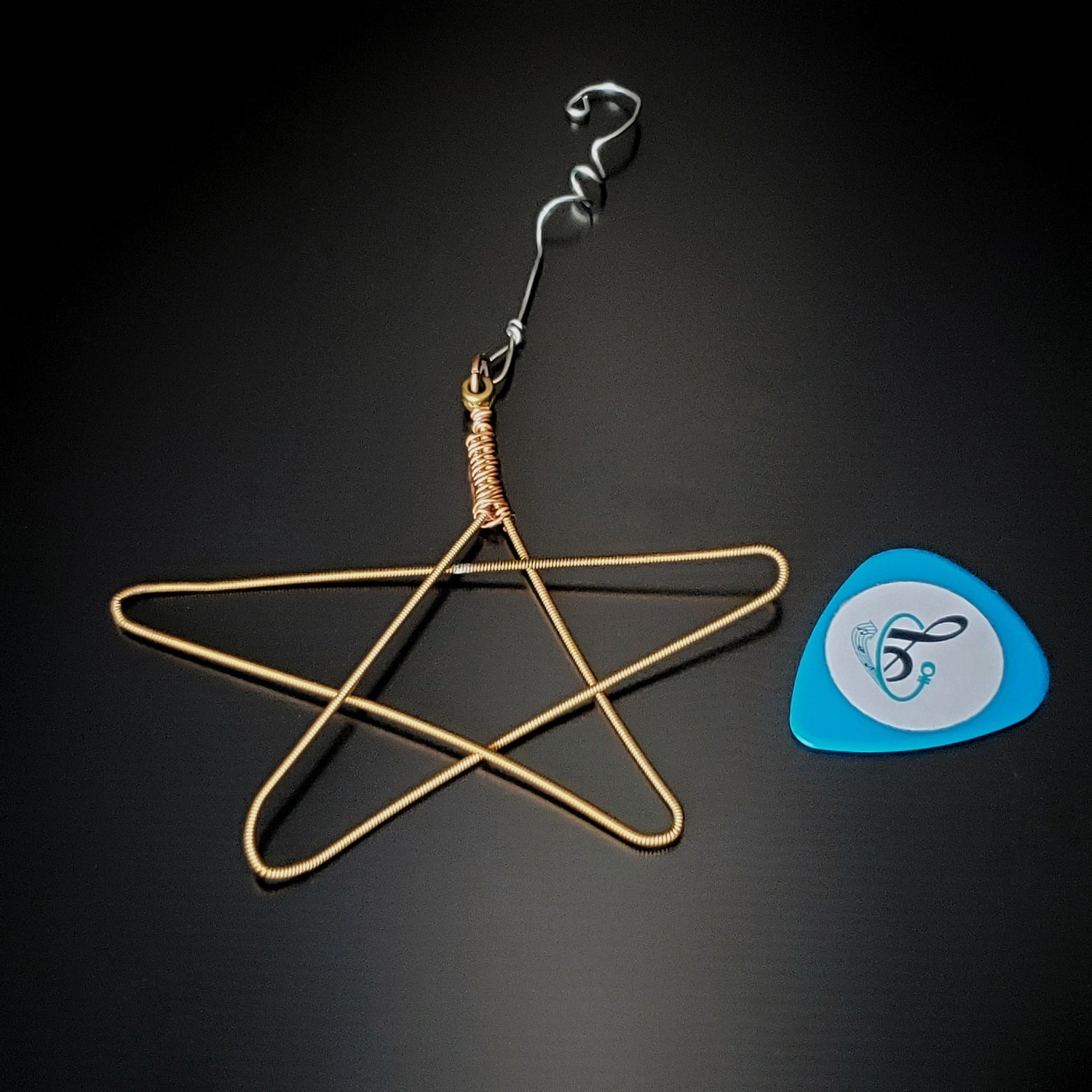 Christmas ornament in the shape of a star, made from an upcycled guitar string next to a guitar pick