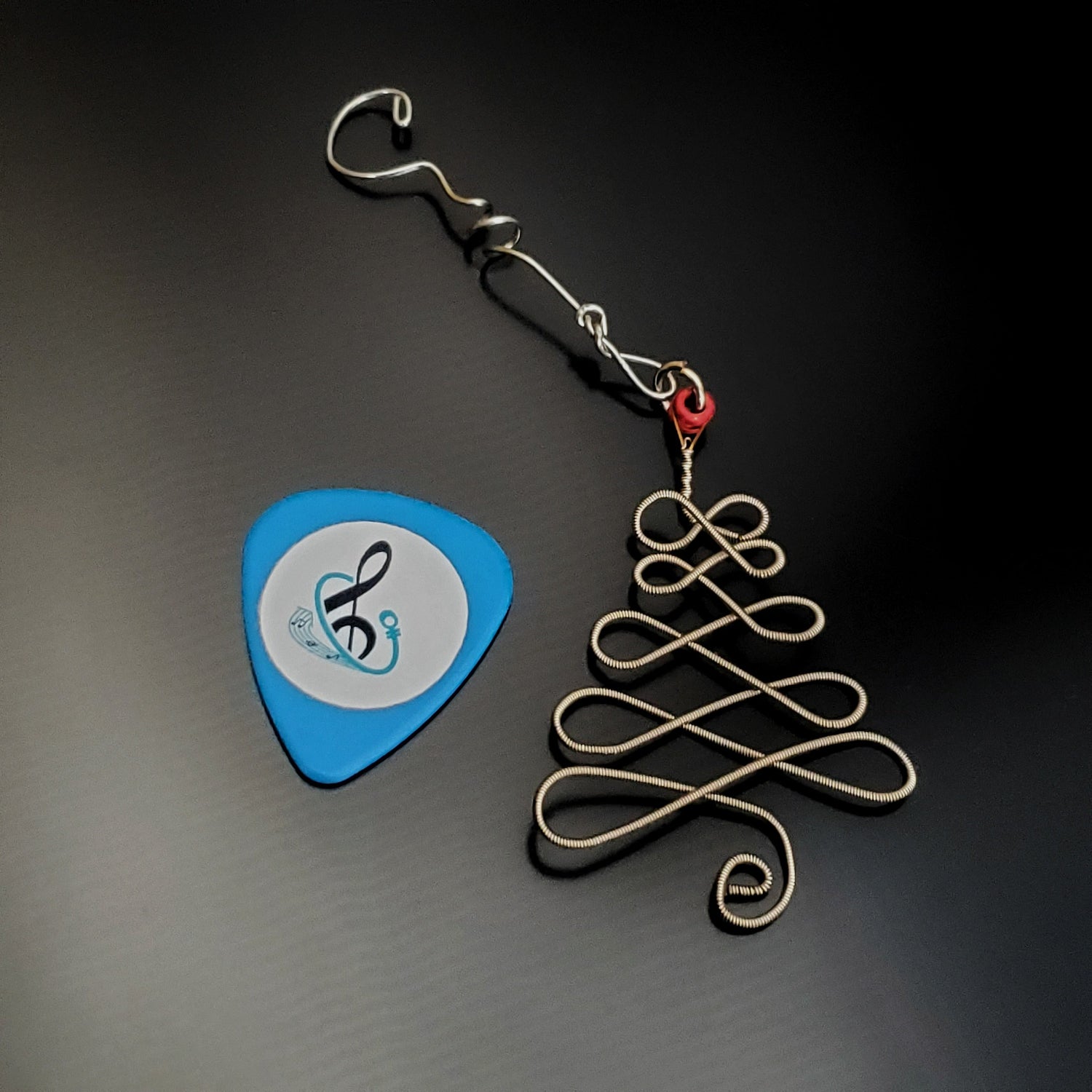 a silver coloured christmas decoration in the shape of a christmas tree made from an upcycled guitar string  next to a light blue guitar pick