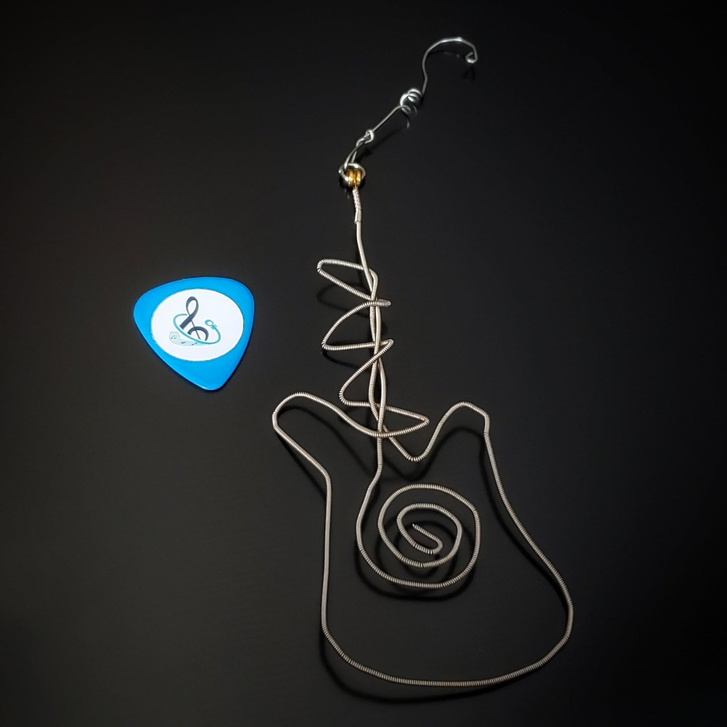 Christmas decoration in the shape of a guitar made from an upcycled guitar string next to a blue guitar pick 