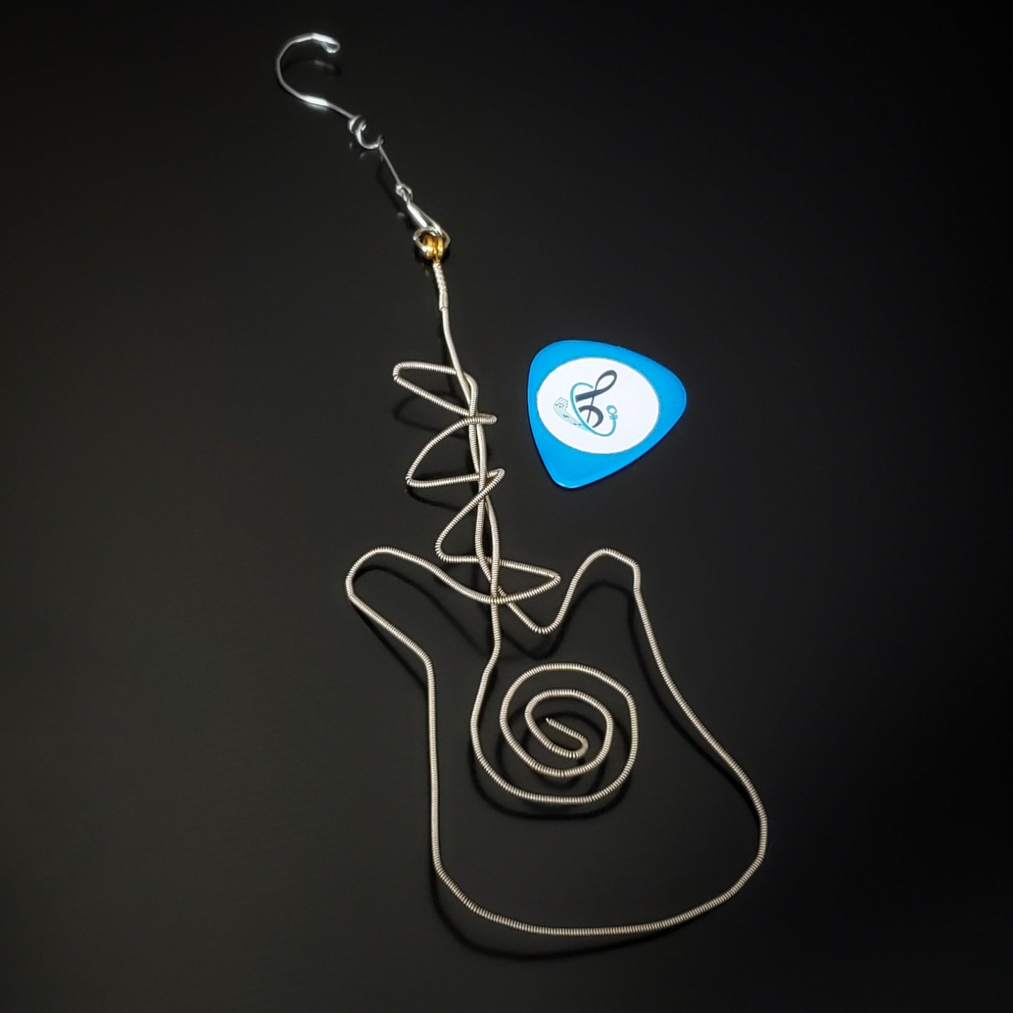 Christmas decoration in the shape of a guitar made from an upcycled guitar string next to a blue guitar pick 
