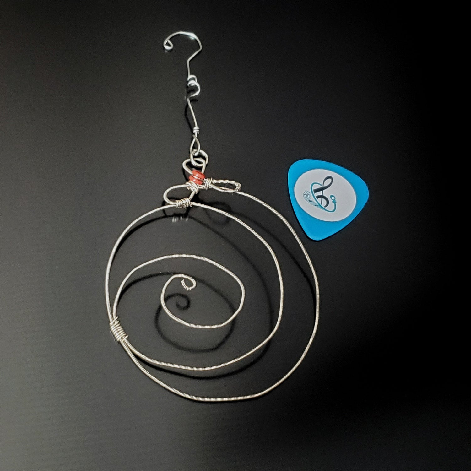 Christmas ornament in the shape of a round swirl made from an upcycled guitar string next to a guitar pick