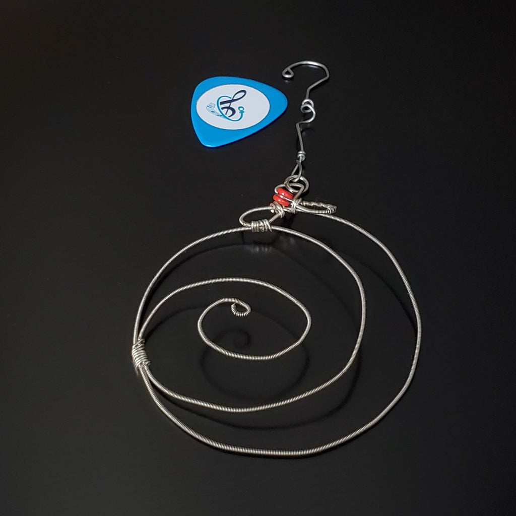 Christmas ornament in the shape of a round swirl made from an upcycled guitar string next to a guitar pick
