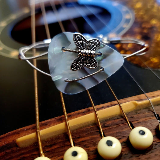 Bracelet made from a multicoloured plectrum and upcycled silver coloured guitar strings with a silver coloured butterfly bead-bracelets is sitting on the bridge of a black guitar 