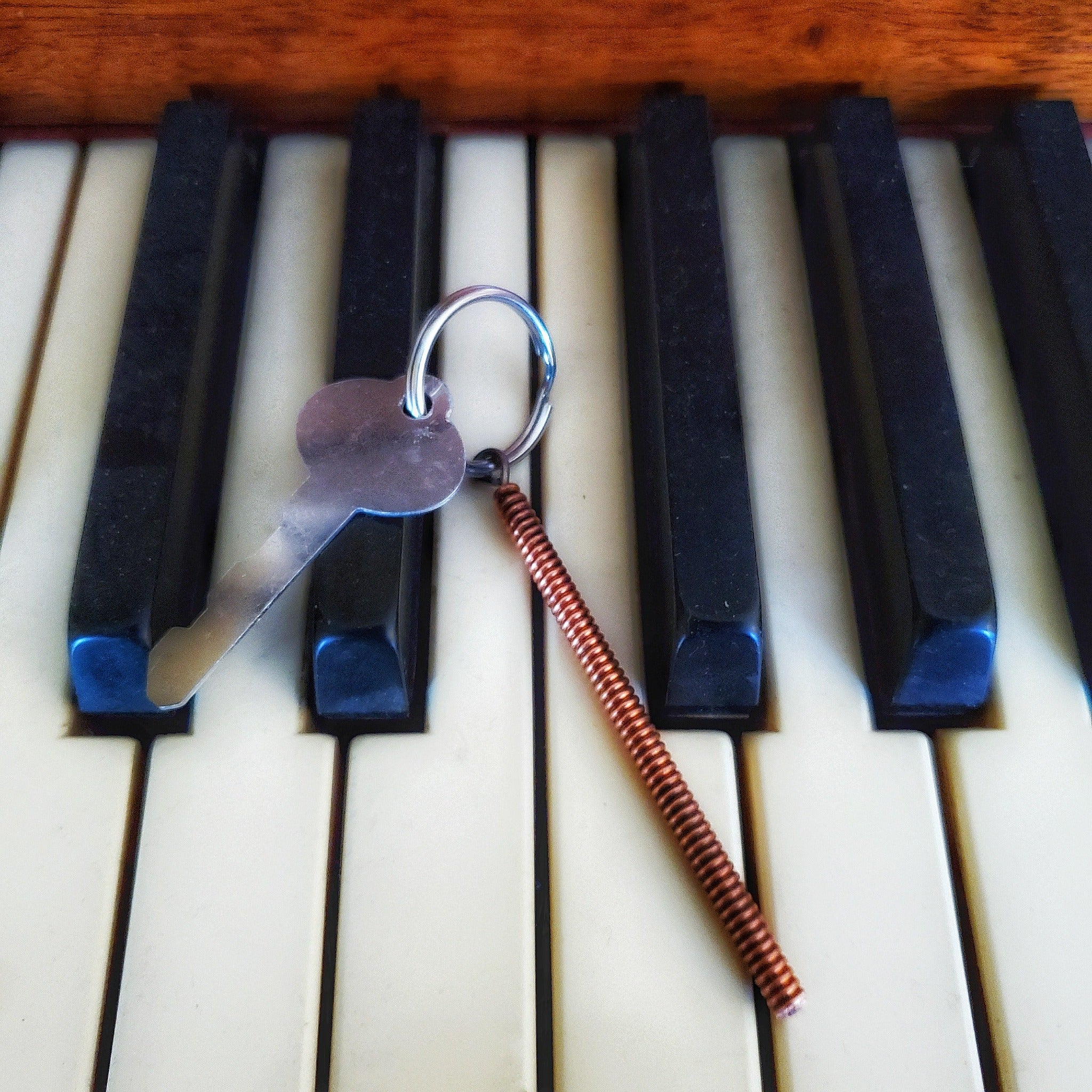 keychain made from a piece of piano string with a key attached, sitting on piano keys