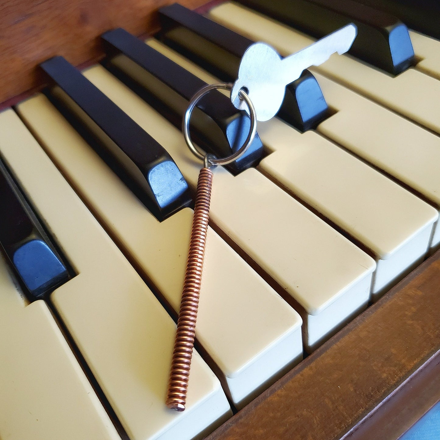 keychain made from a piece of piano string with a key attached, sitting on piano keys