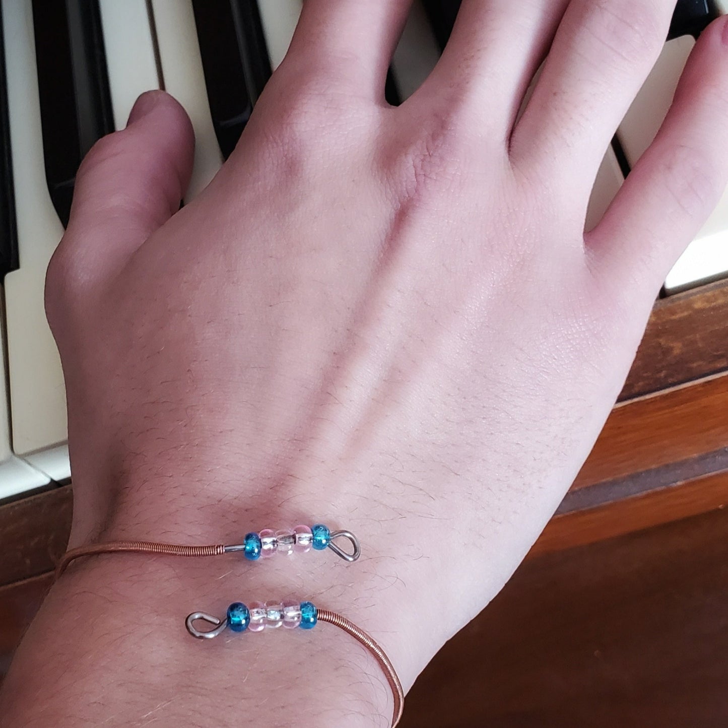 hand wearing bracelet with beads representing the colours of the trans pride flag 