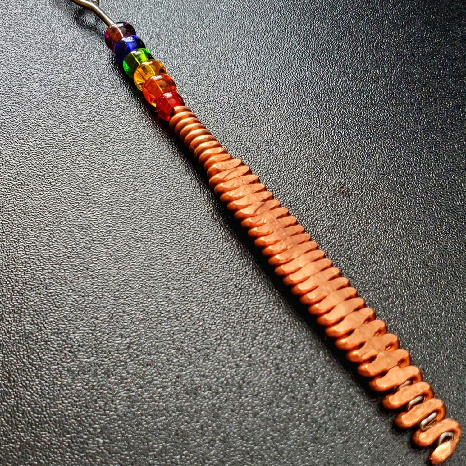Close-up of a hammered piano string pendant with 6 LGBTQ flag coloured beads with chain on a piano