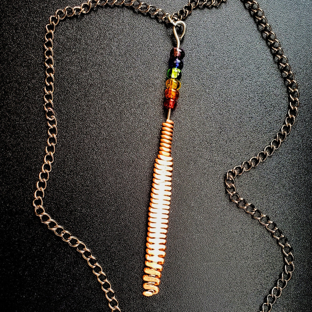 Hammered piano string pendant with 6 LGBTQ flag coloured beads with chain on a piano black background 
