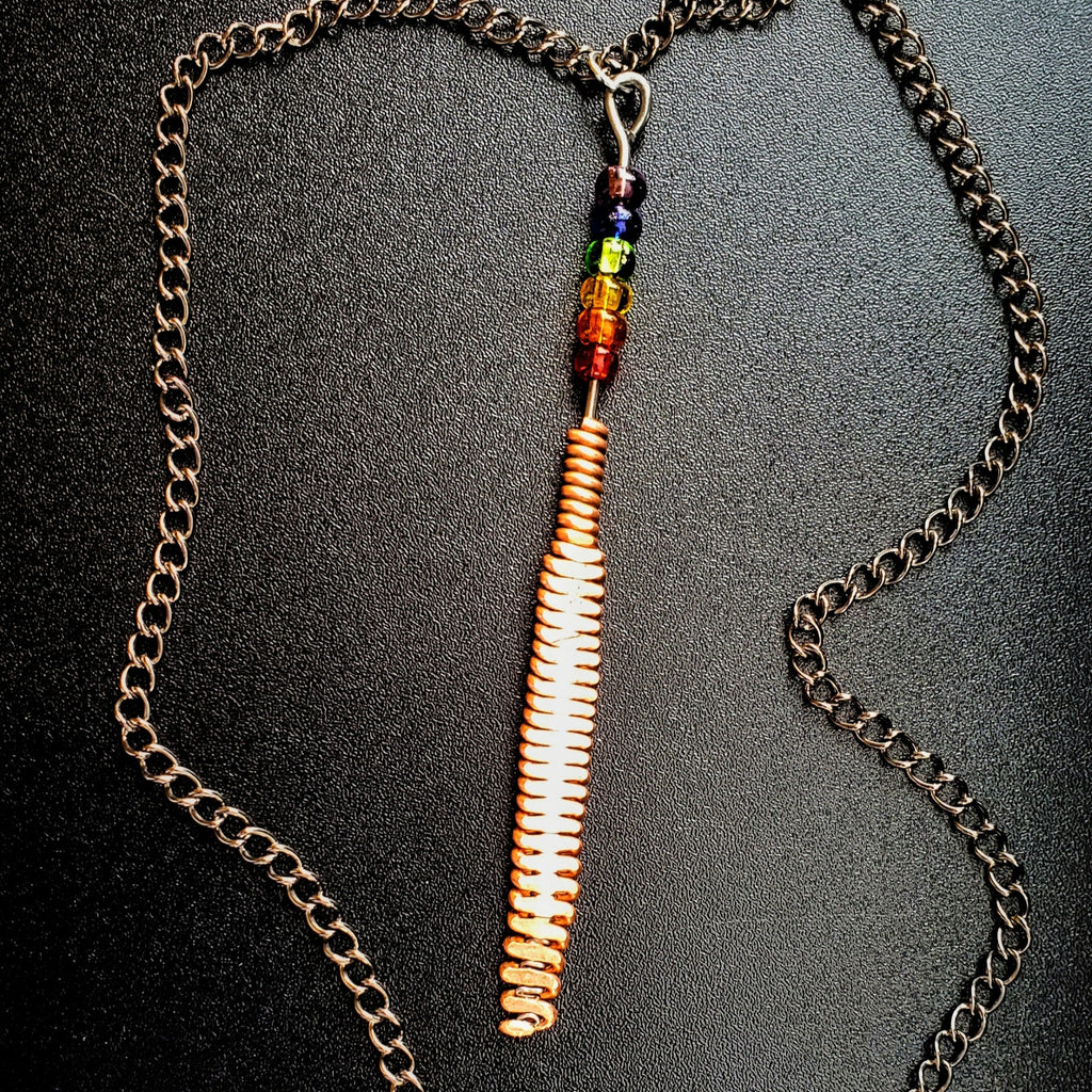 Hammered piano string pendant with 6 LGBTQ flag coloured beads with chain on a piano black background 