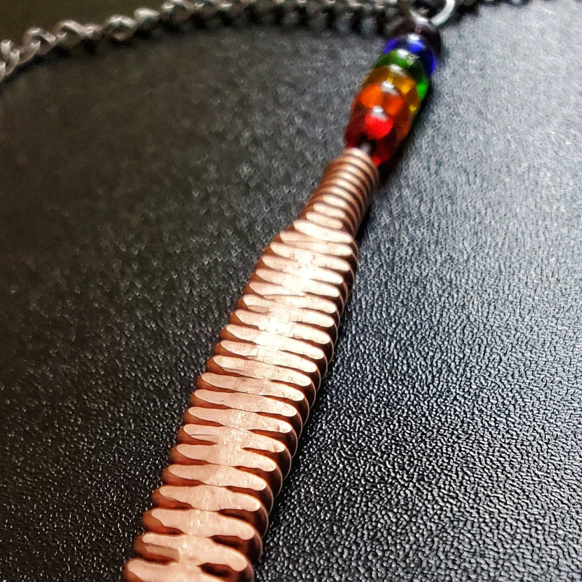 Close-up of a hammered piano string pendant with 6 LGBTQ flag coloured beads with chain on a piano