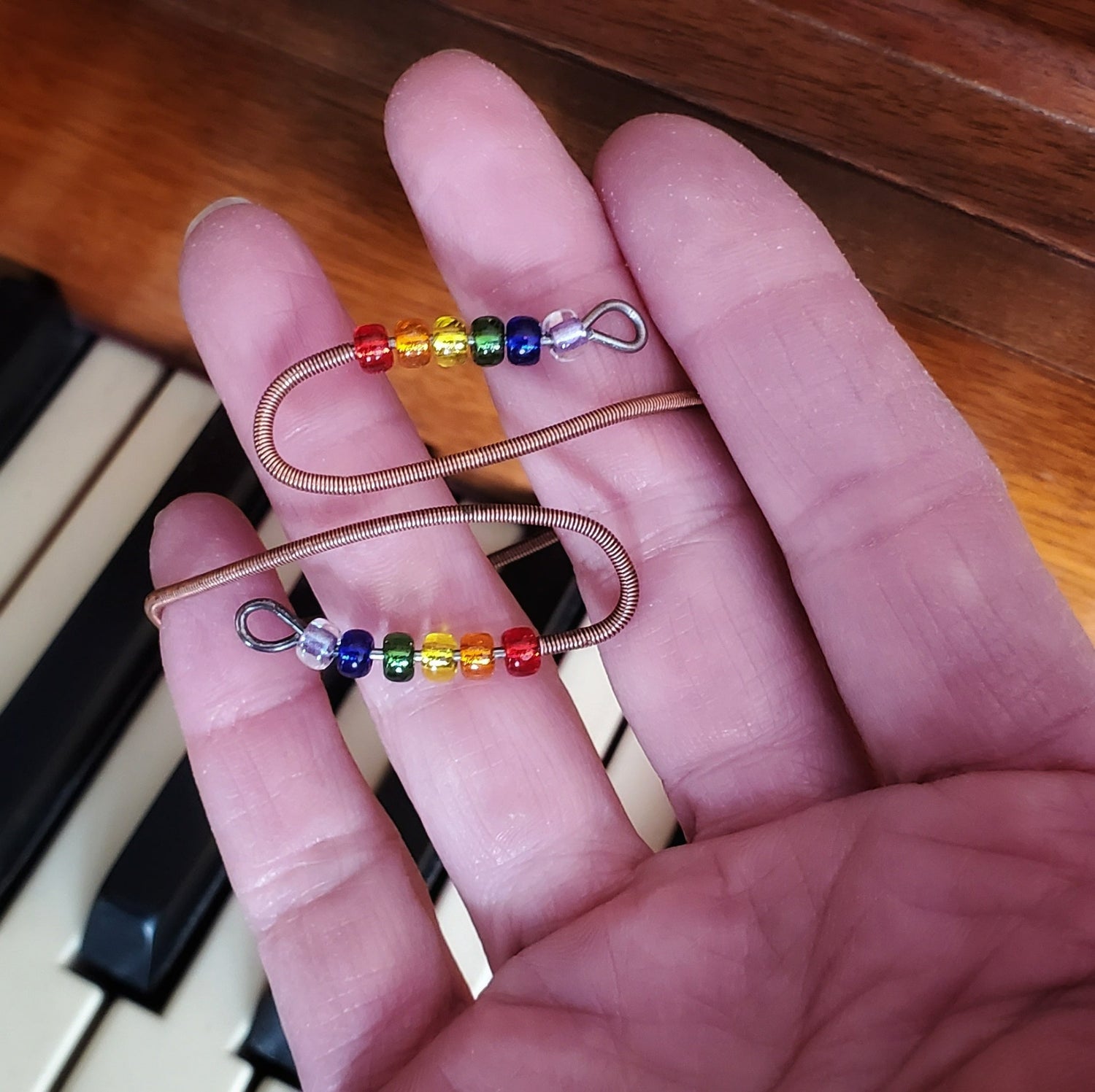 hand holding a cuff style bracelet made from upcycled piano strings and beads representing the LGBTQ pride flag