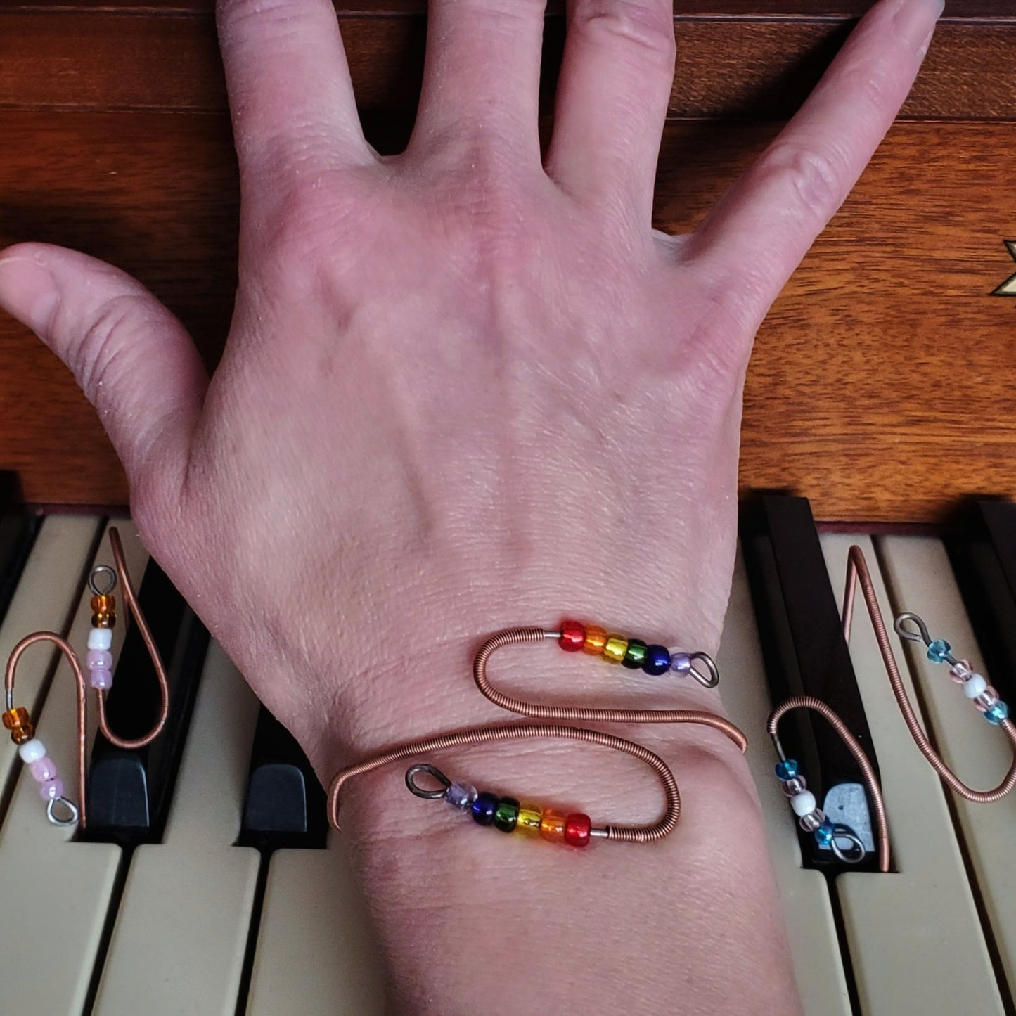 hand on piano keys with 3 bracelets representing various pride flags