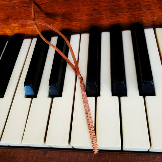 bookmark made from a hammered piano string and a piece of rust coloured suede sitting on a piano keyboard