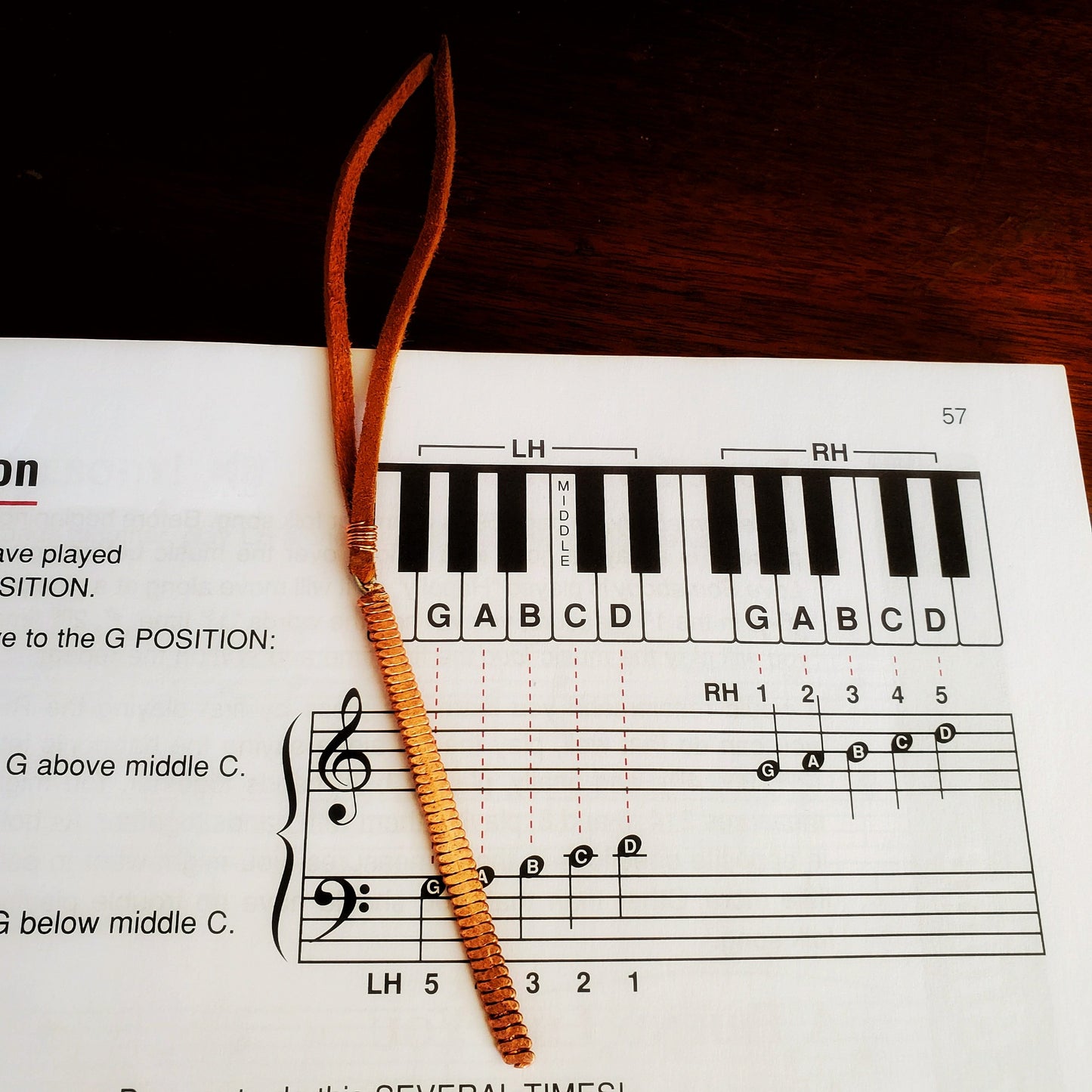 bookmark made from a hammered piano string and a piece of rust coloured suede sitting on the page of a book with music notes and words written in black on white background