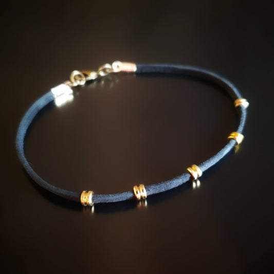 bracelet made from black suede cord and gold coloured guitar string ballends on a black background