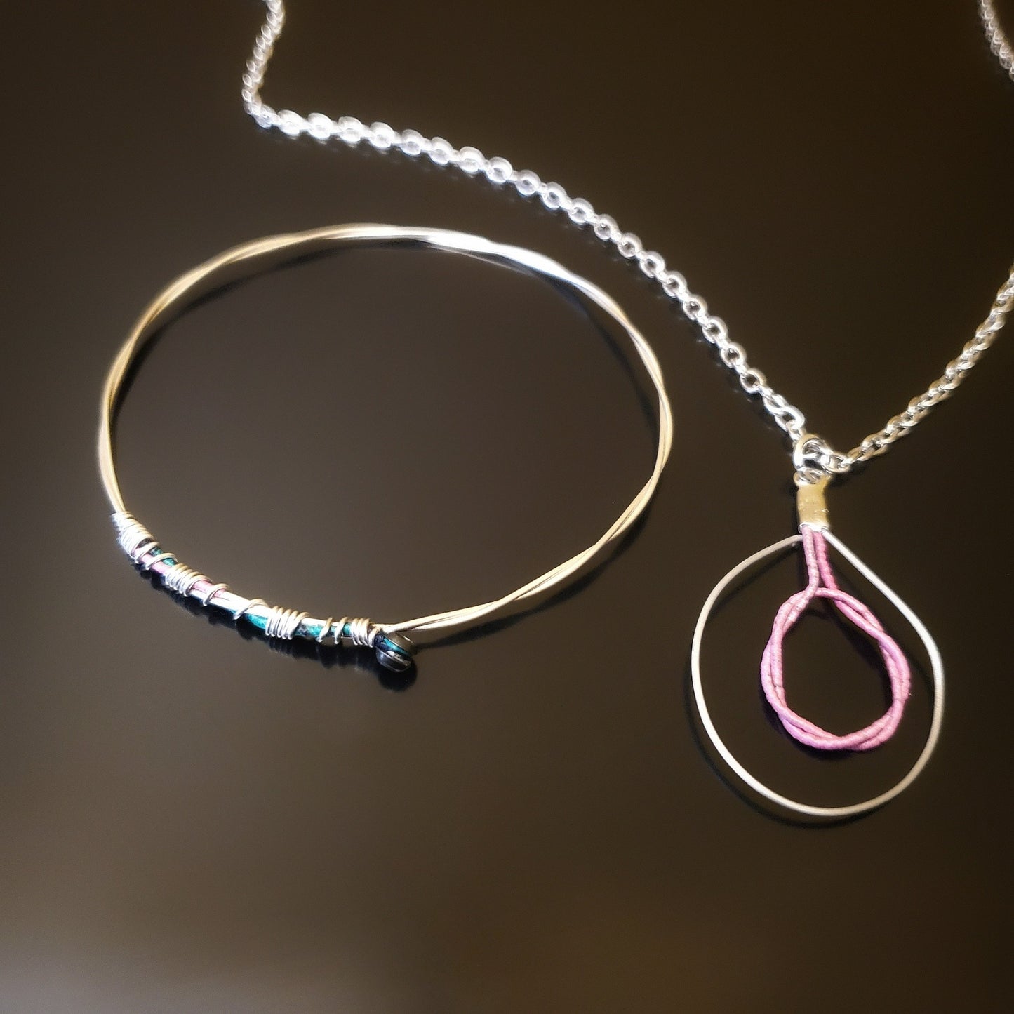 bangle style bracelet and necklace with pink and silver colours on black background