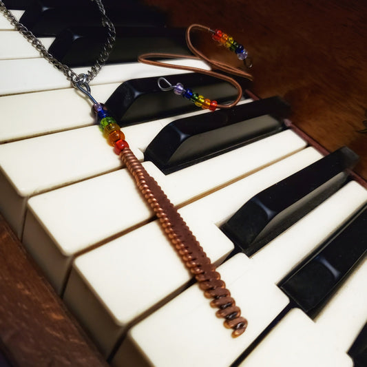 necklace and bracelet made from upcycled piano strings with beads representing the LGBTQ pride flag, sitting on piano keys
