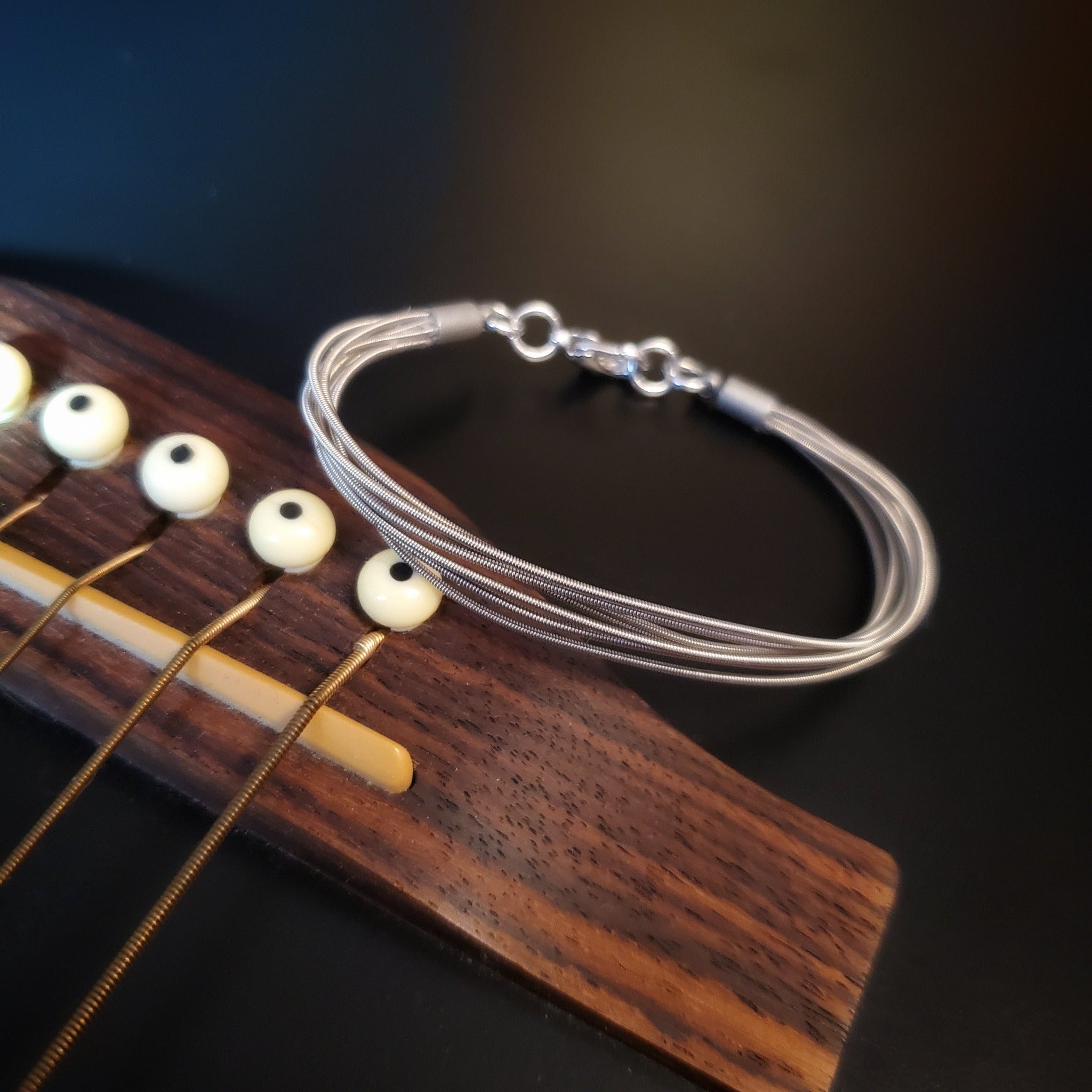 multistrand guitar string clasp style bracelet sitting on the body of a black guitar