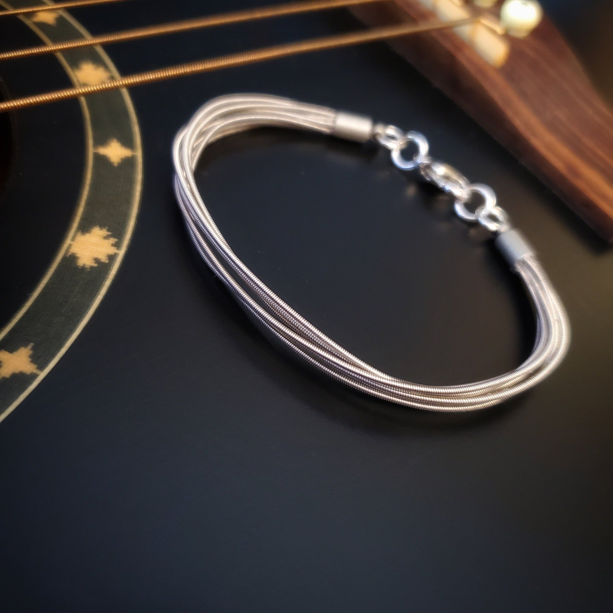 multistrand guitar string clasp style bracelet sitting on the body of a black guitar