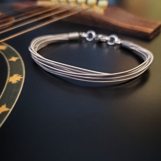 multistrand guitar string clasp style bracelet sitting on the body of a black guitar