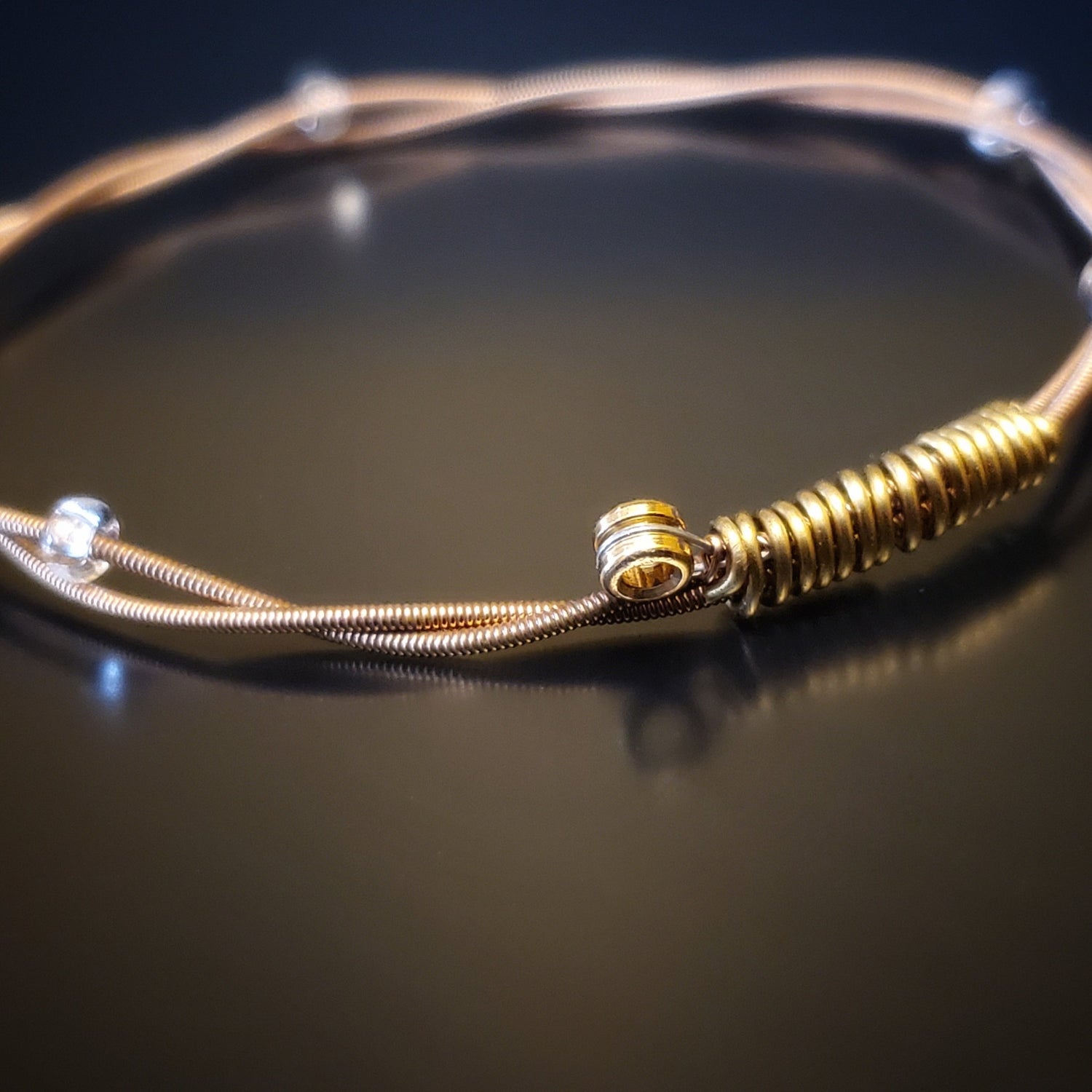 copper coloured bangle style guitar string bracelet with clear glass beads with black background