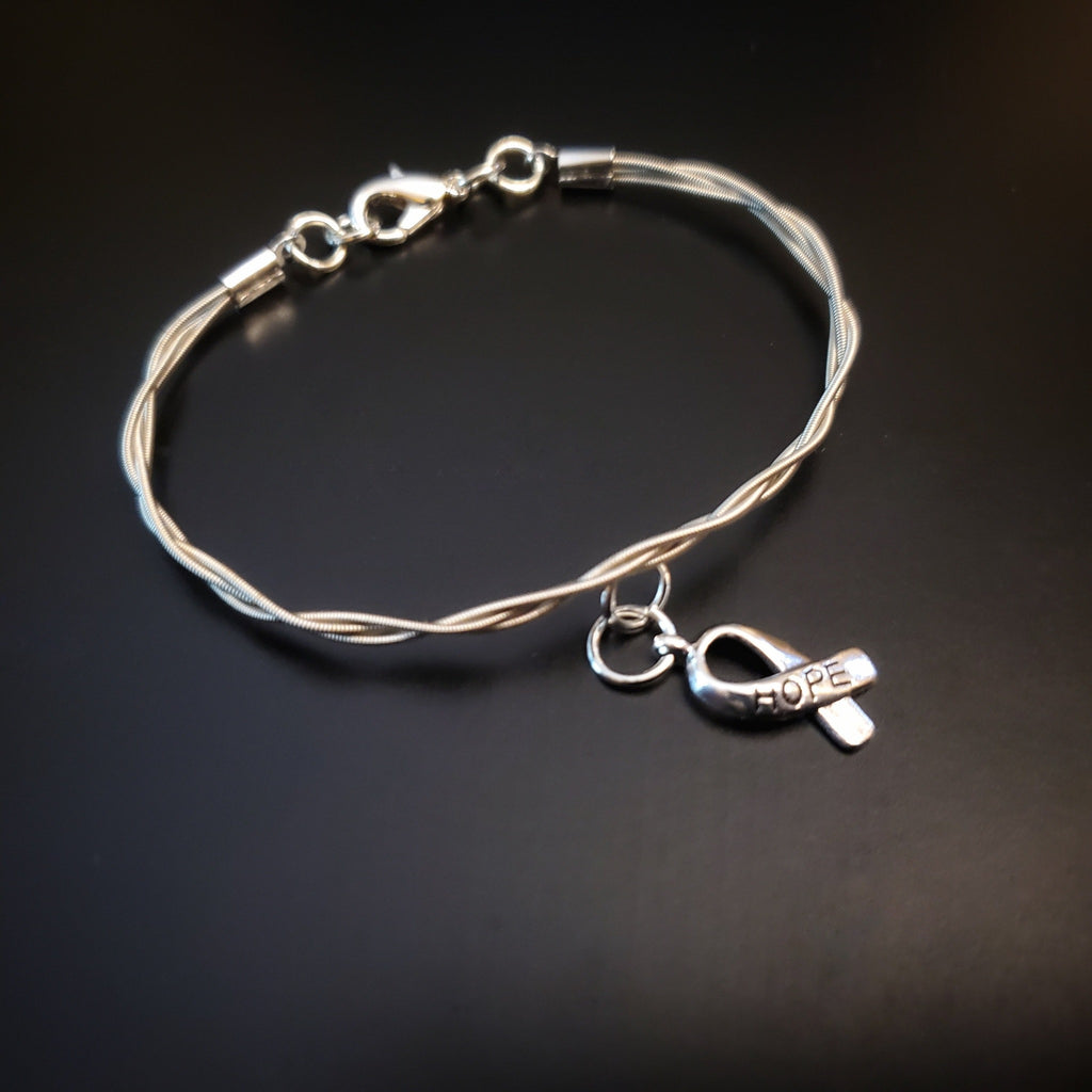 braided guitar string clasp style bracelet with ribbon style charm the word "HOPE" is engraved on the charm - black background