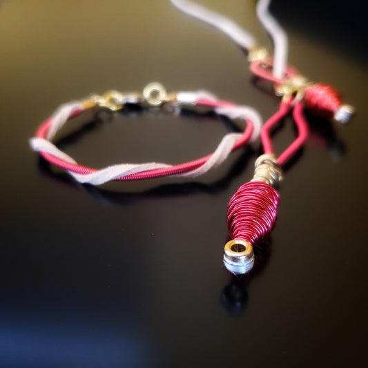 closeup of an upcycled harp string and suede necklace and bracelet on a black background