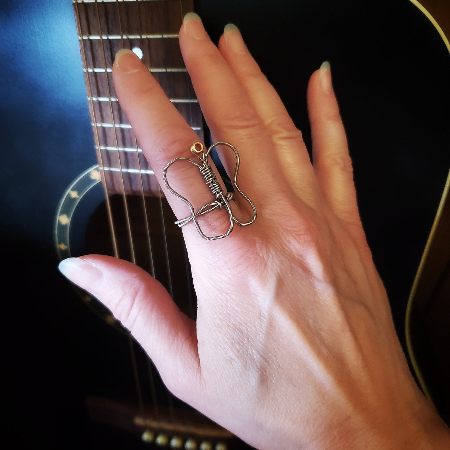 hand resting against a black guitar wearing a butterfly shaped guitar string ring