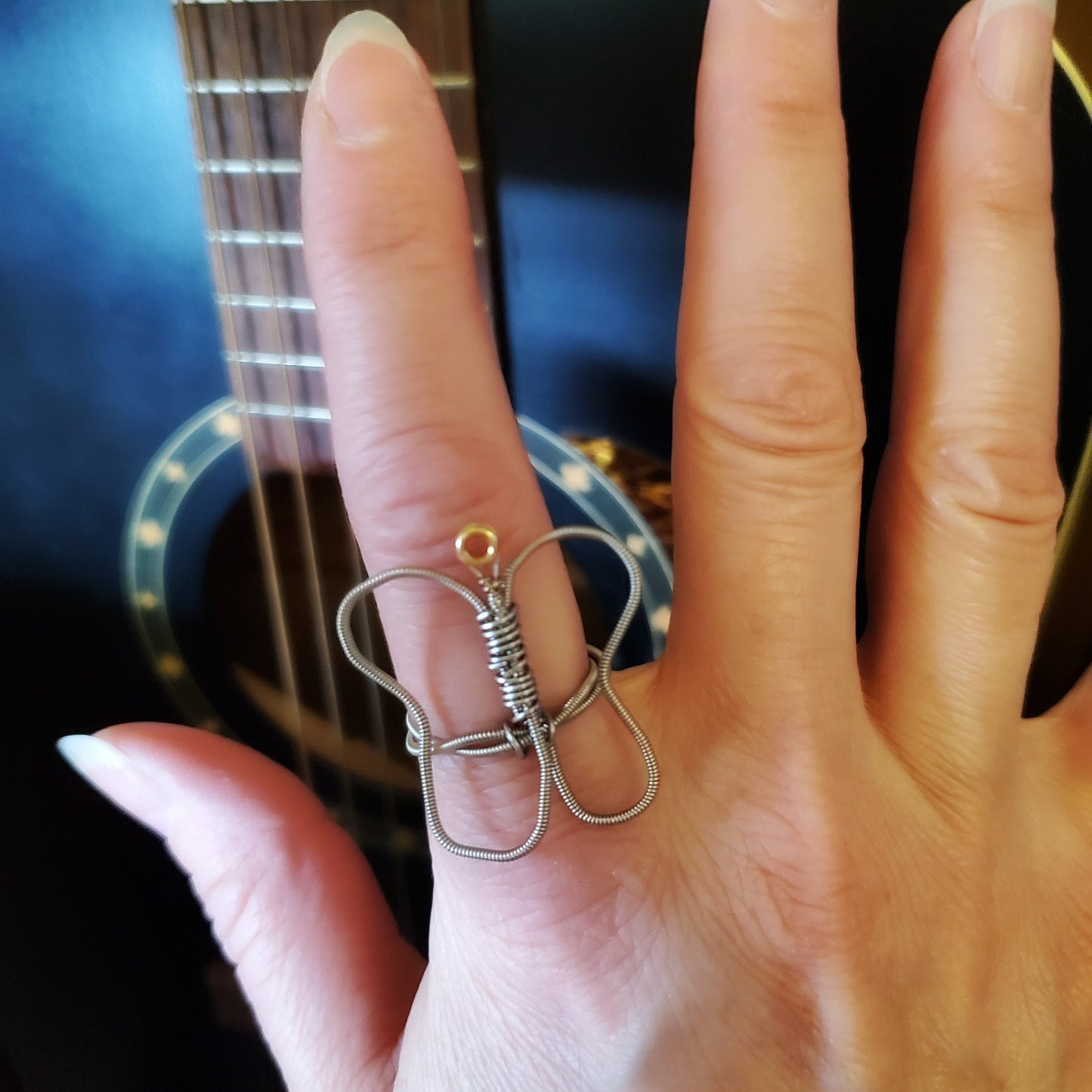 hand resting against a black guitar wearing a butterfly shaped guitar string ring