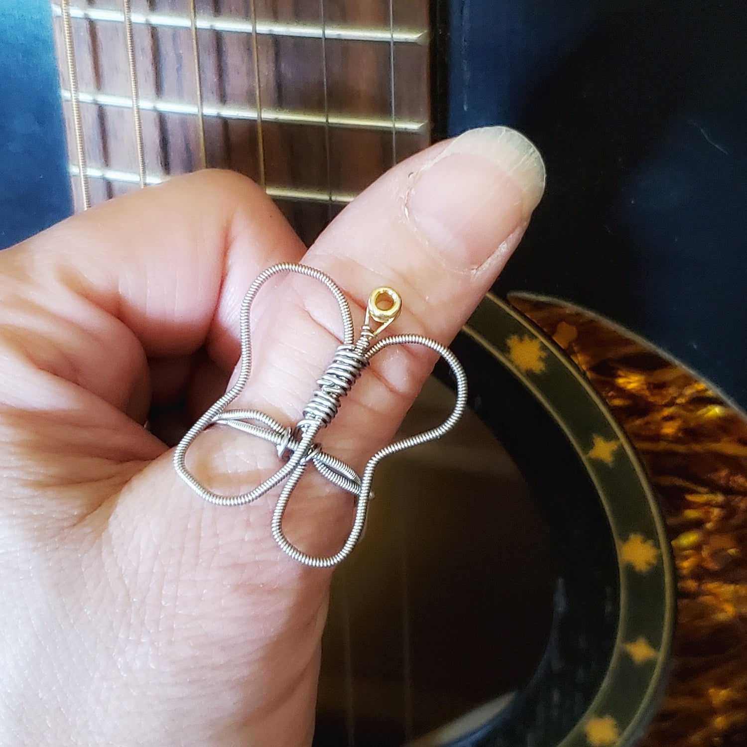 thumb resting against a black guitar wearing a butterfly shaped guitar string ring