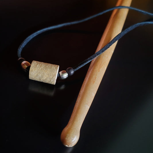 Upcycled Drumstick and Black Suede Necklace With Smooth Silver Beads lying on a drumstick