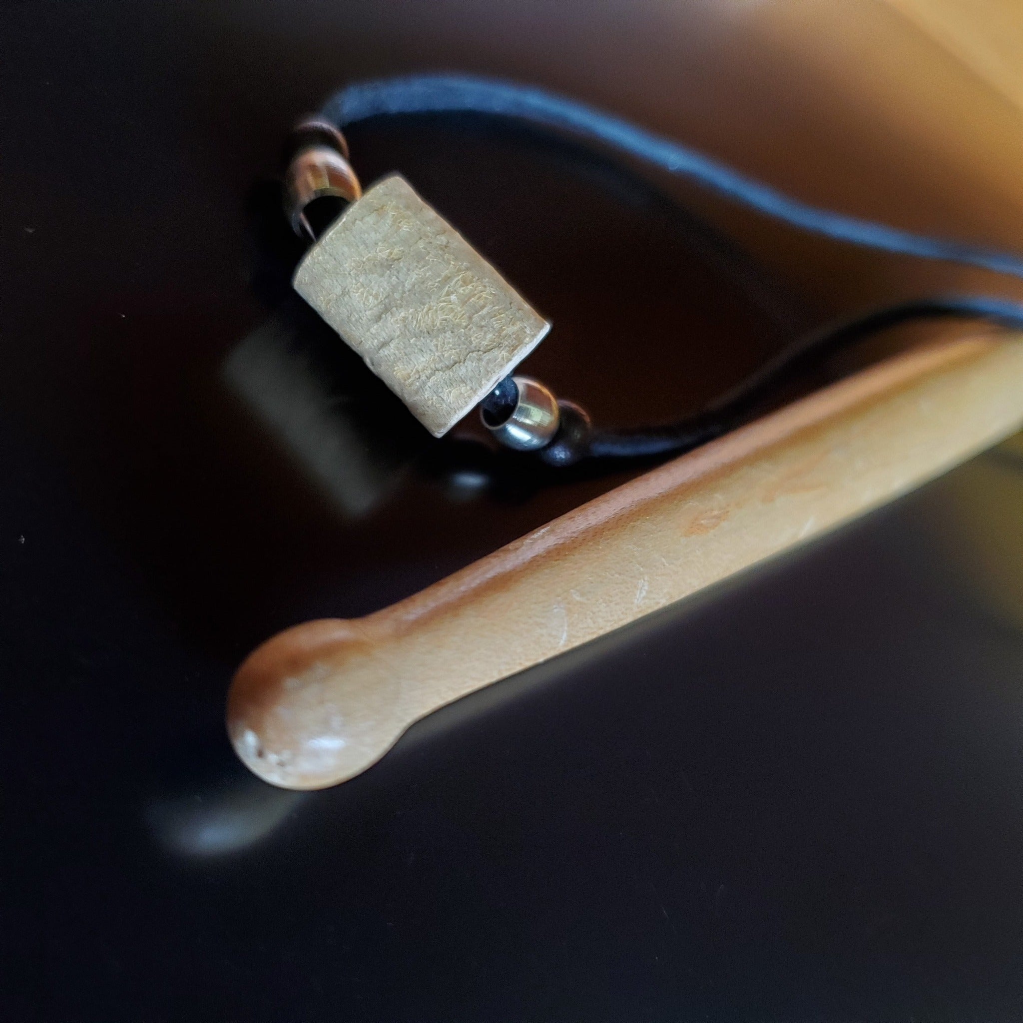 Upcycled Drumstick and Black Suede Necklace With Smooth Silver Beads lying on a drumstick