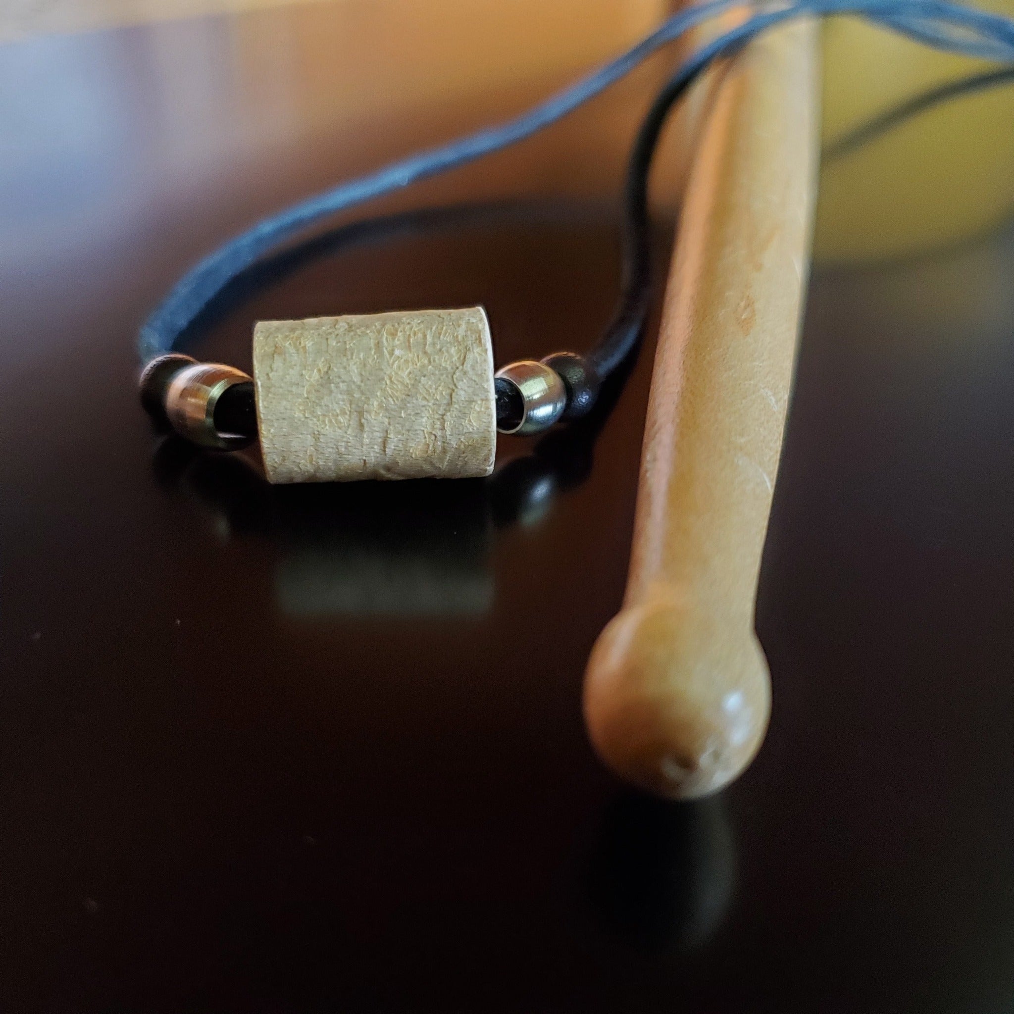 Upcycled Drumstick and Black Suede Necklace With Smooth Silver Beads lying on a drumstick