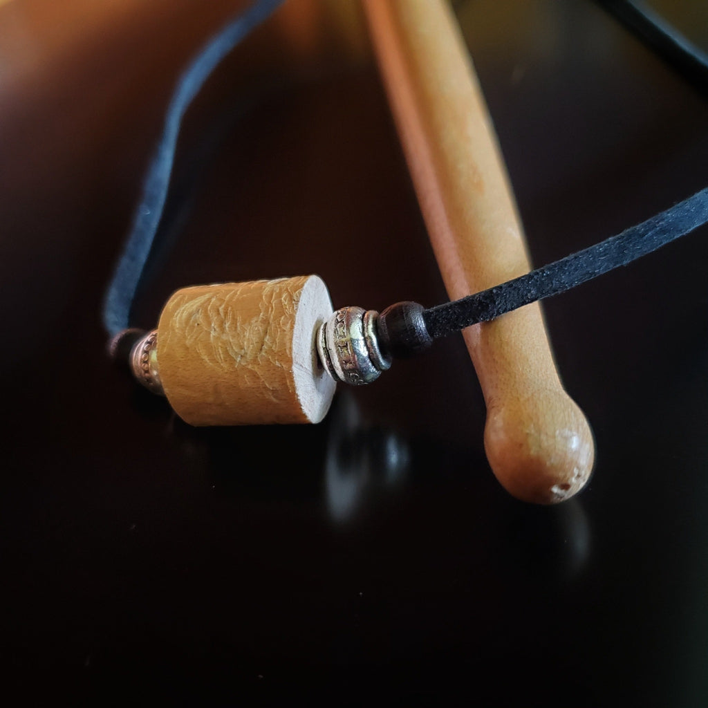 Upcycled Drumstick and Black Suede Necklace With Accented Silver Bead lying on a drumstick
