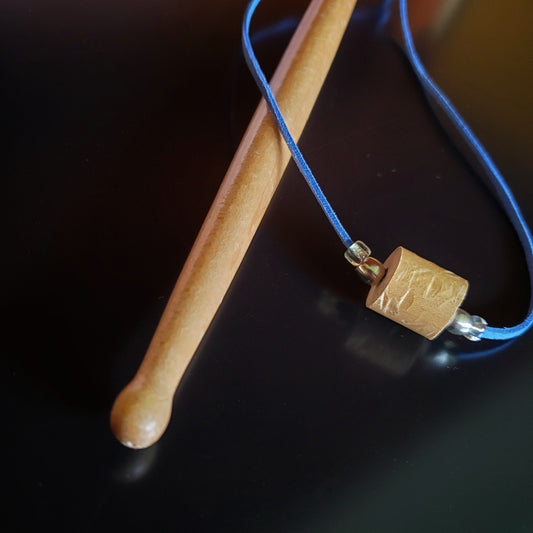 Upcycled Drumstick and Blue Faux-Suede Necklace With Smooth Silver Beads lying on a drumstick