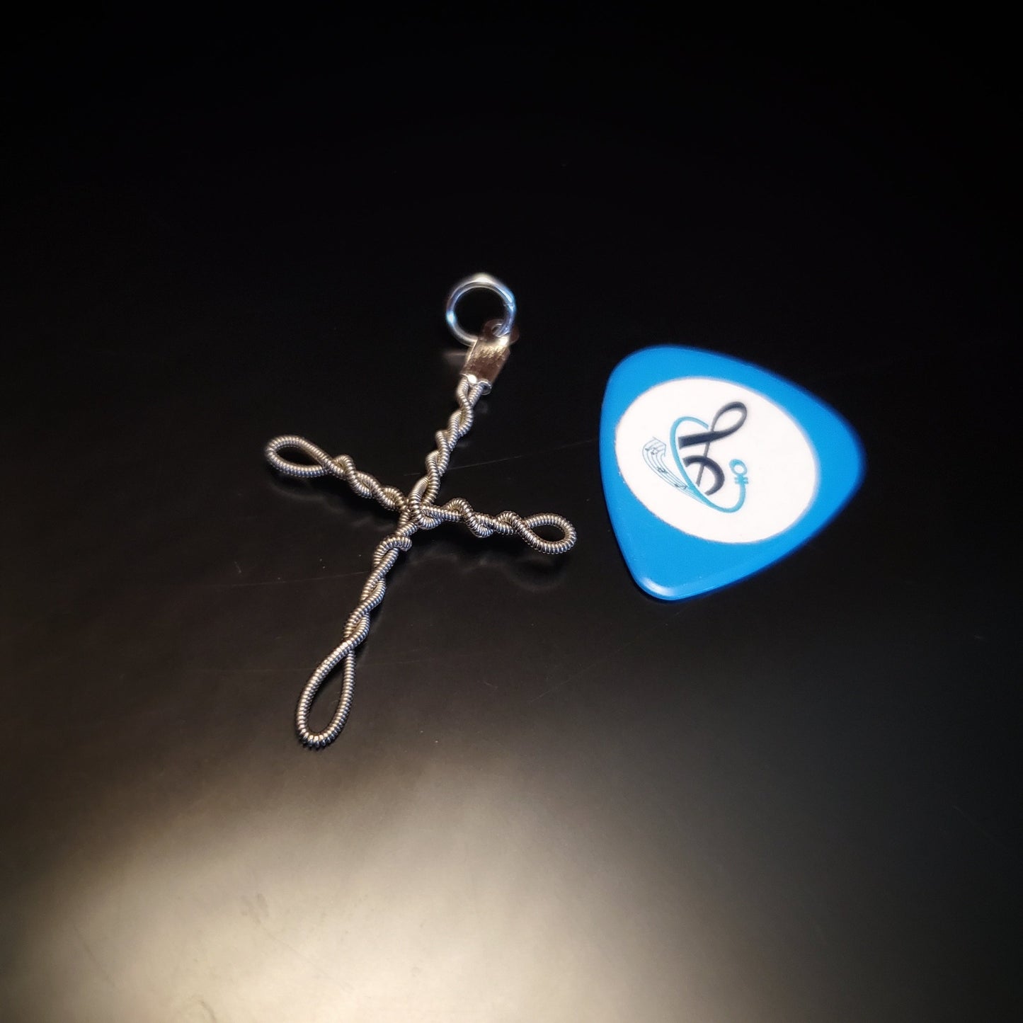 Upcycled guitar string cross style pendant next to a blue guitar pick