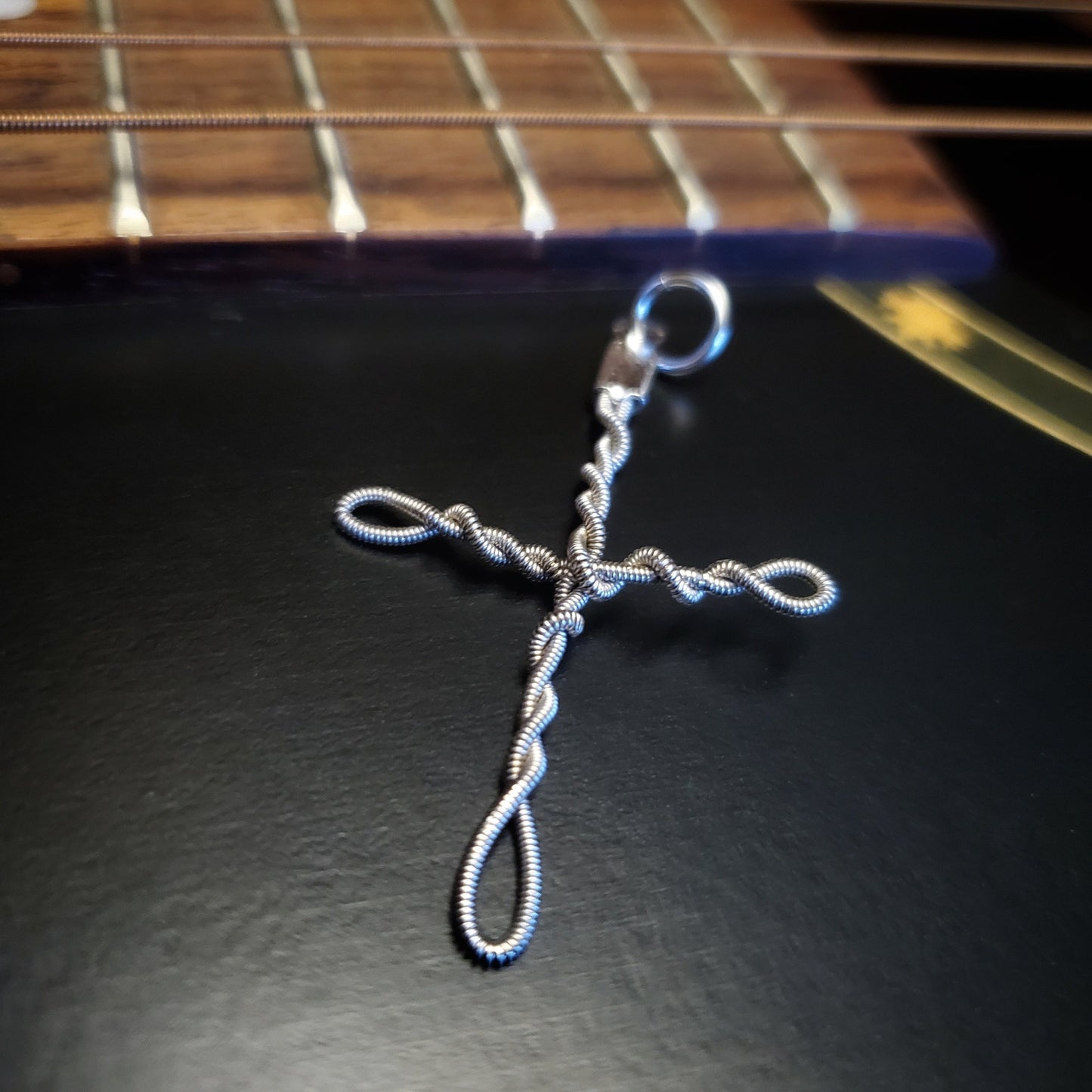 Upcycled guitar string cross style pendant lying near the bridge of a guitar 