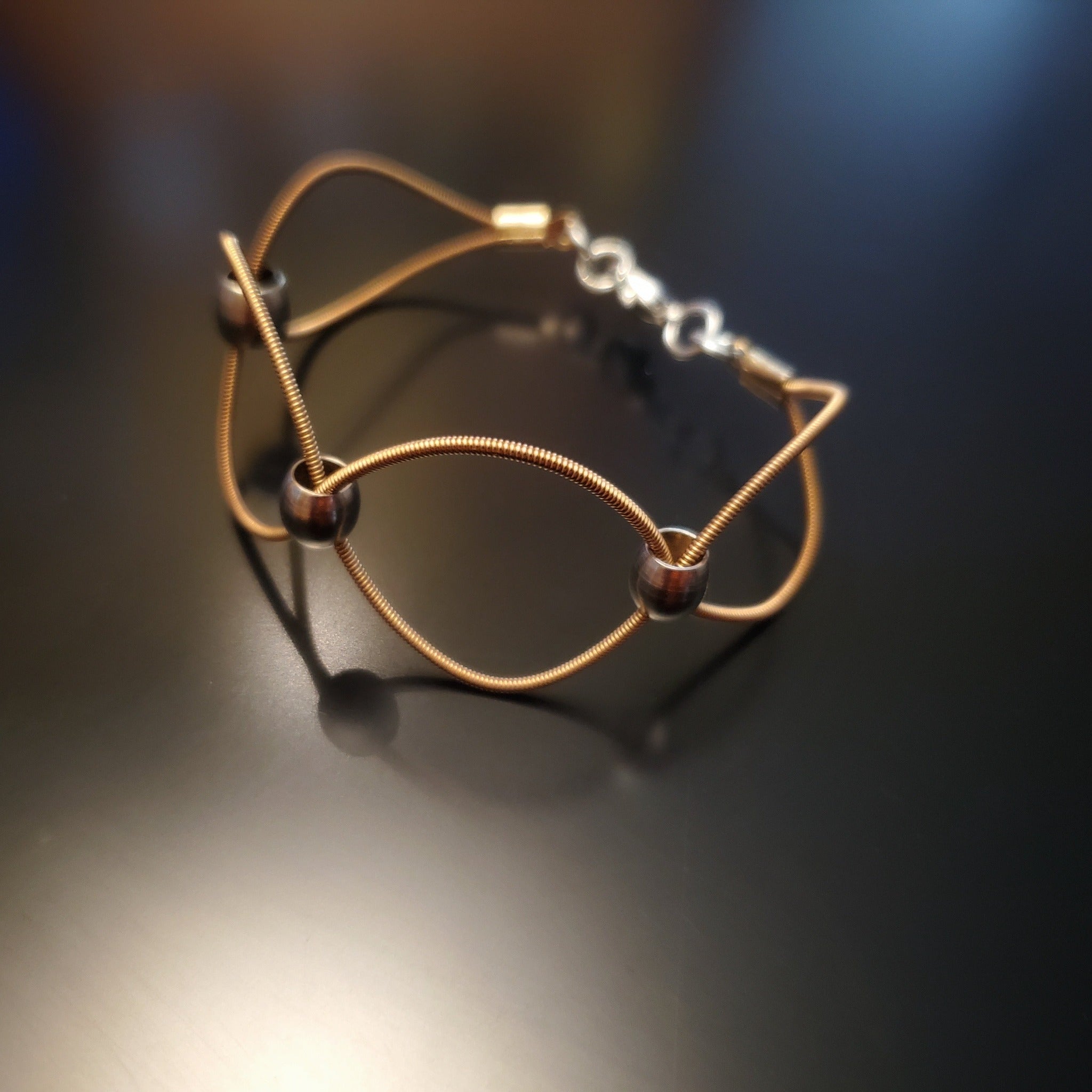 upcycled guitar strings bracelet with silver coloured beads on a black background