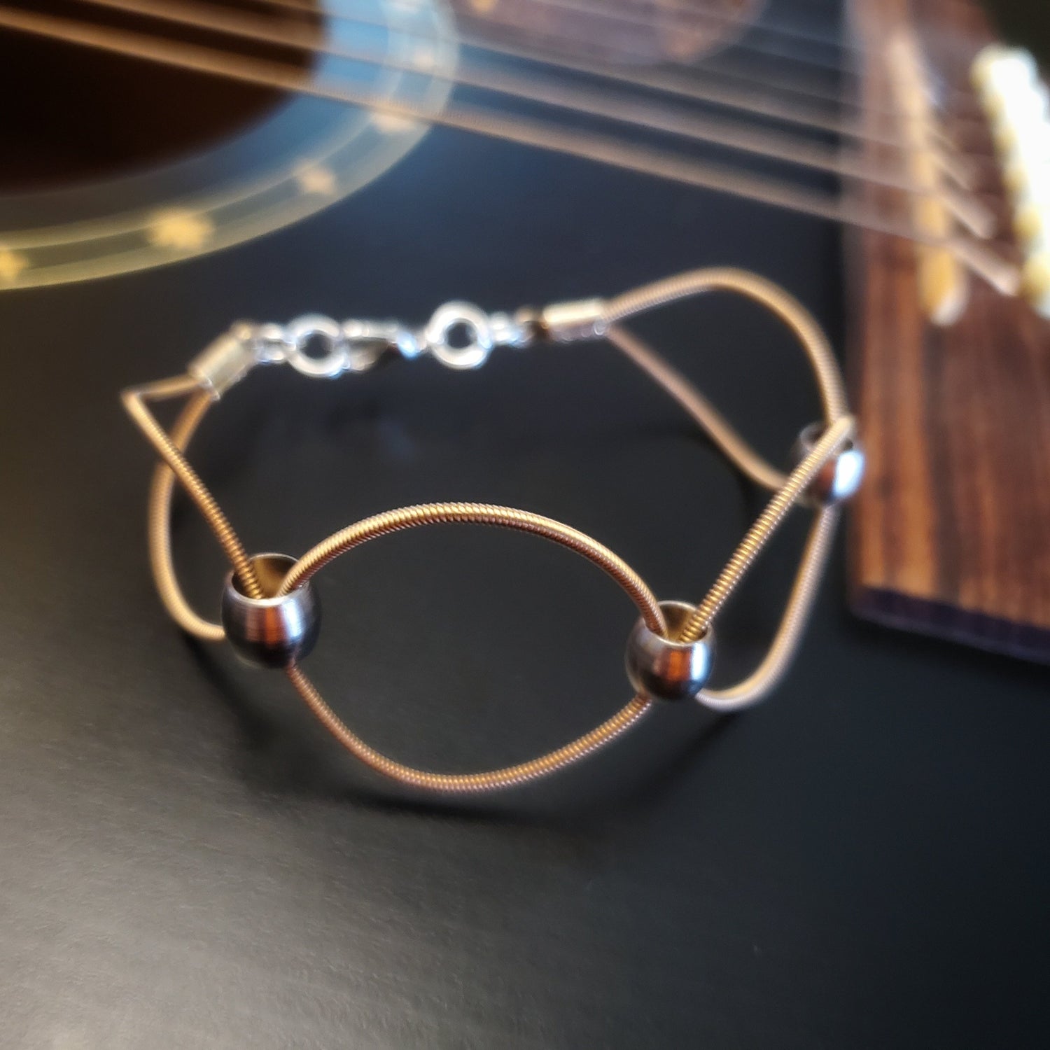 upcycled guitar strings bracelet with silver coloured beads on a black guitar