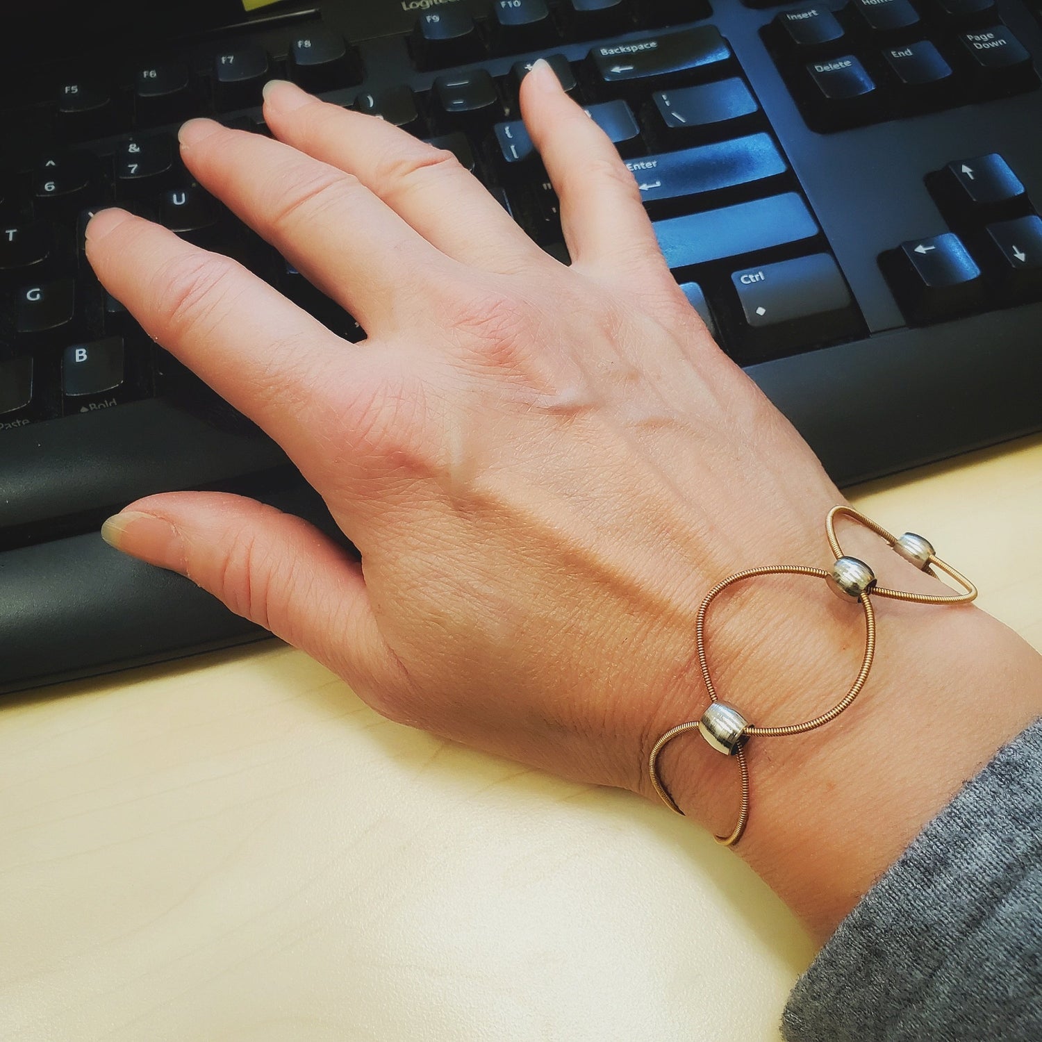 hand resting on a keyboard - on wrist is a upcycled guitar strings bracelet with silver coloured beads 