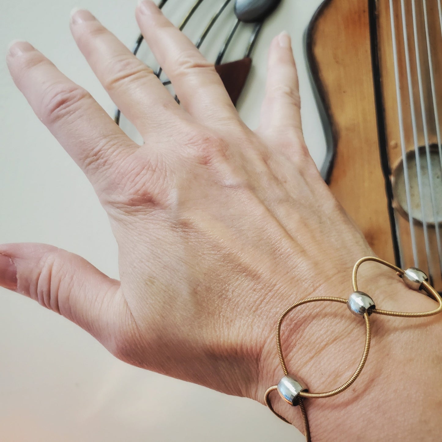 hand - on the wrist is a upcycled guitar strings bracelet with silver coloured beads with a guitar in the background