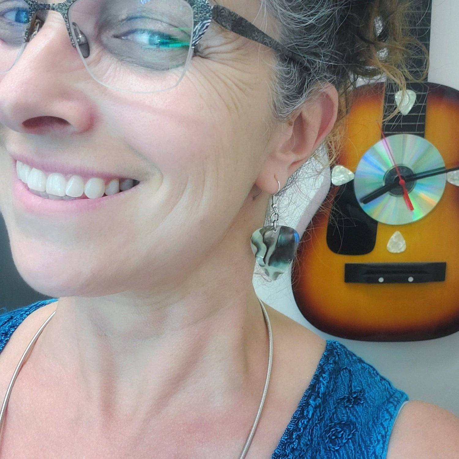 woman wearing guitar pick earrings with a guitar clock in the background