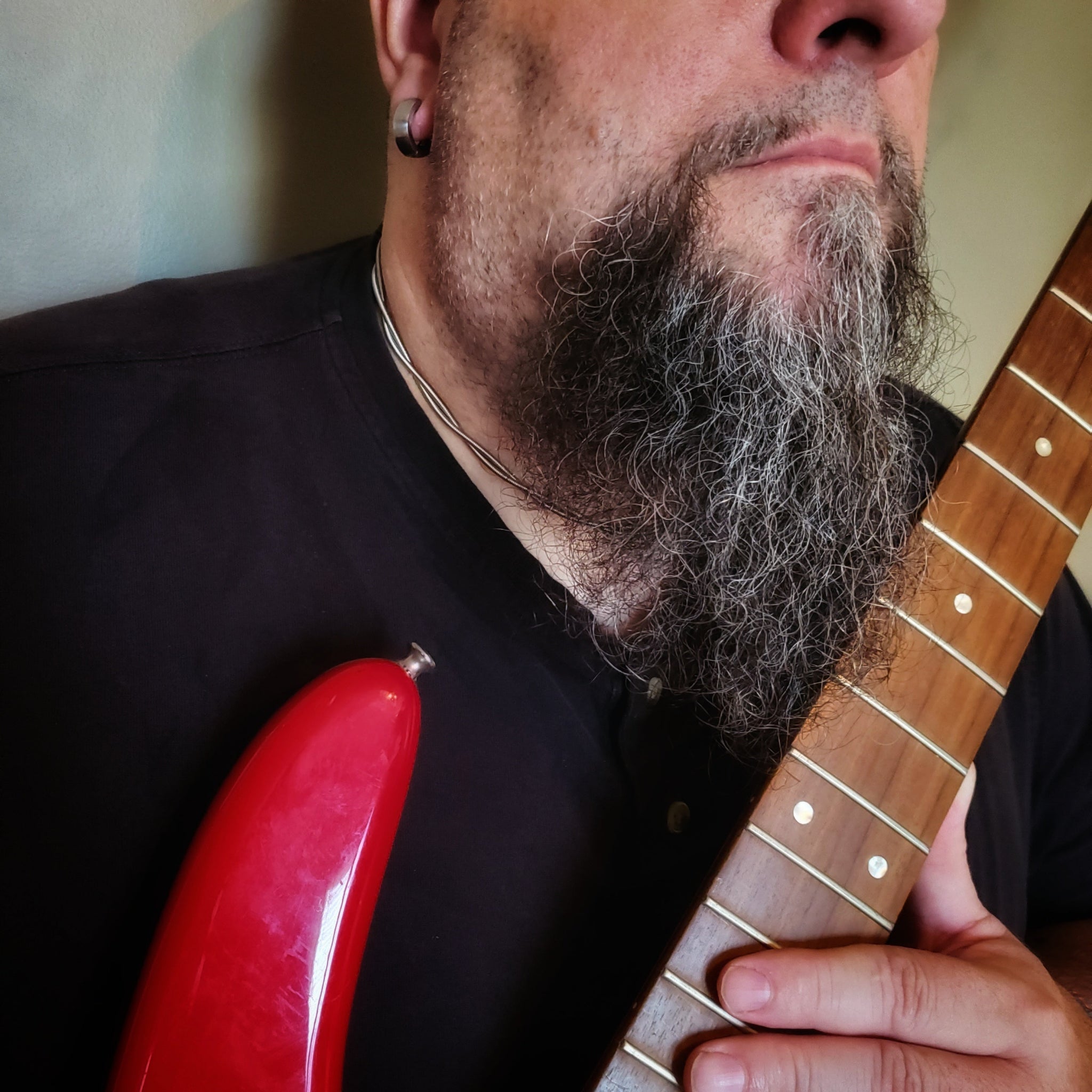 man wearing a chain made from bass guitar strings, holding a red electric bass