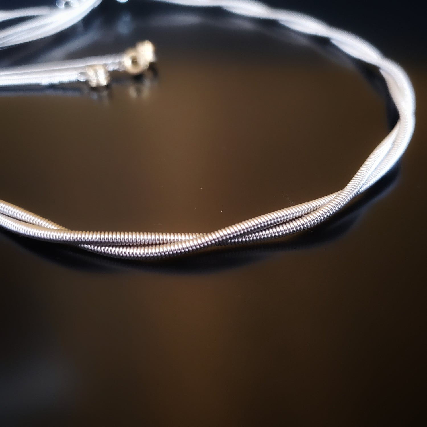 Closeup of silver coloured bass guitar string necklace- black background 