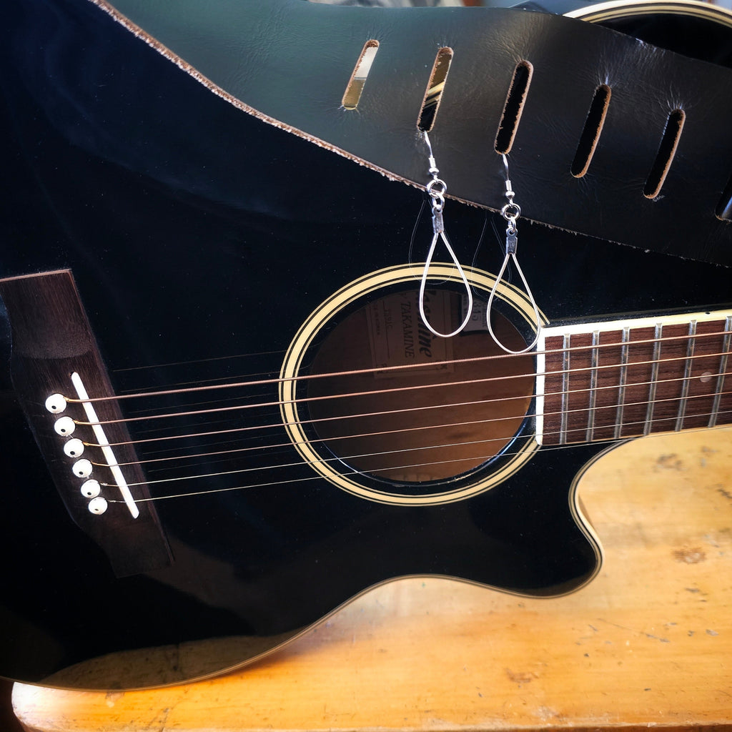 Black acoustic guitar with a pair of guitar string teardrop earrings hanging from its neck