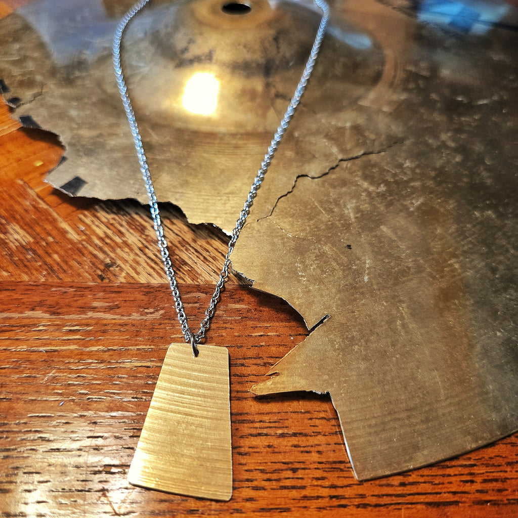 Close-up of Close-up of Upcycled Rectangle Shaped Cymbal Piece Necklace beside Broken Cymbal