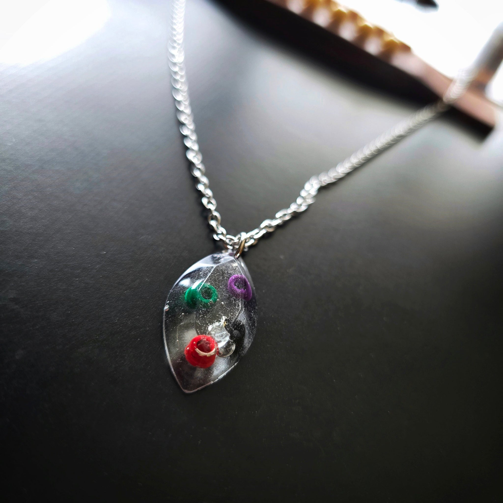 Close-up of Marquise Shaped Resin Pendant with Multicoloured Ballends Necklace on Black Guitar