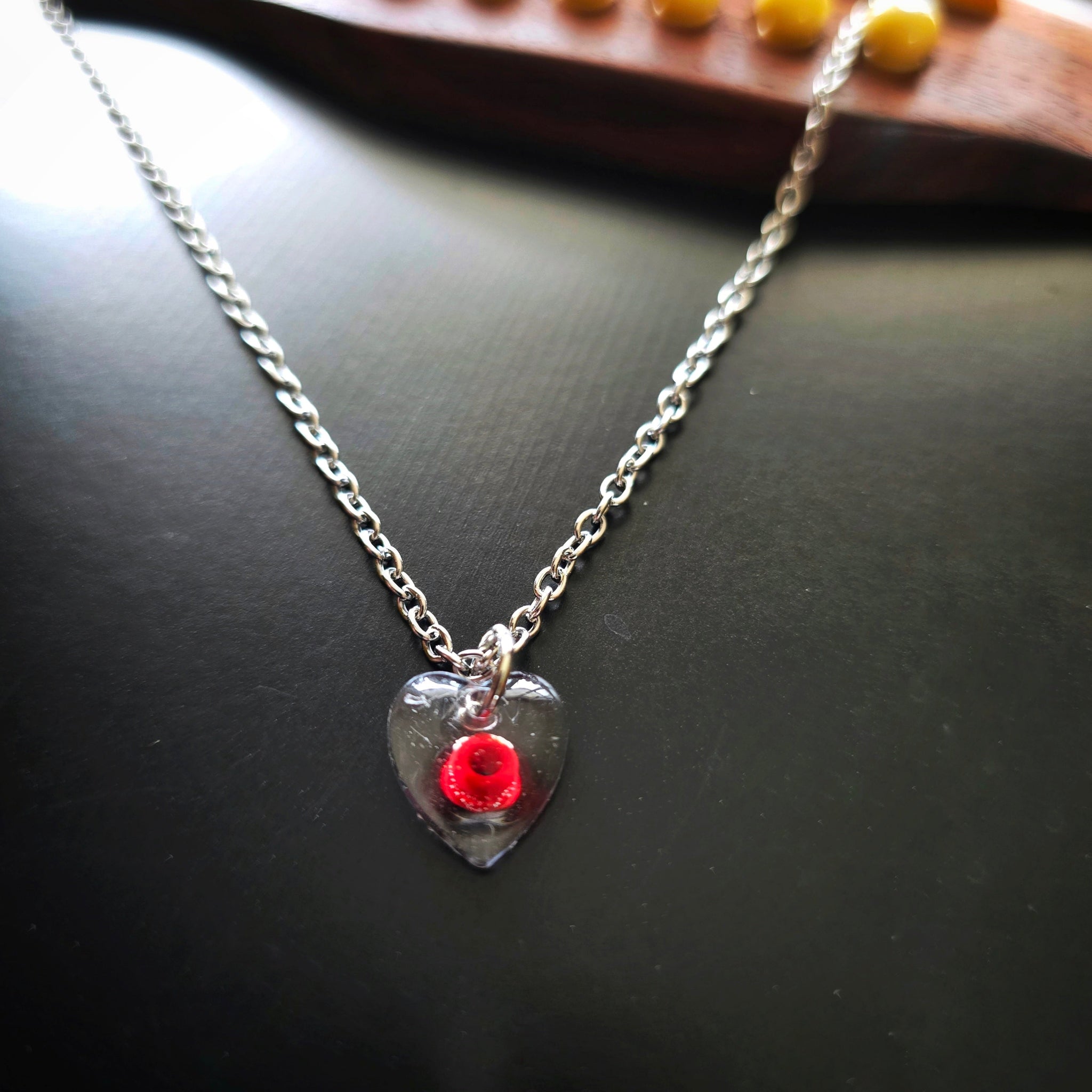Close-up of Silver necklace with a red ballend in a resin heart-shaped pendant on a guitar
