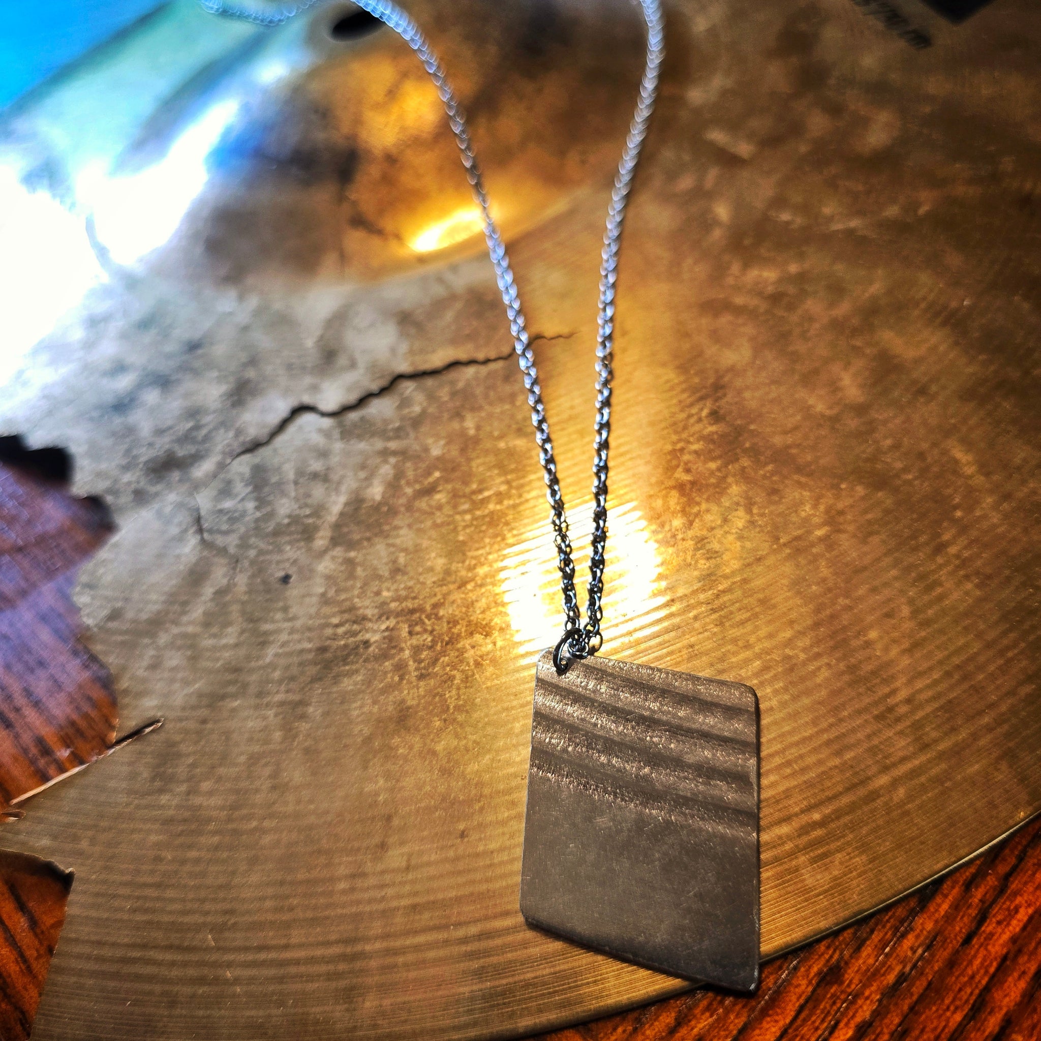 Close-up of Upcycled Diamond Shaped Cymbal Piece Necklace beside Broken Cymbal