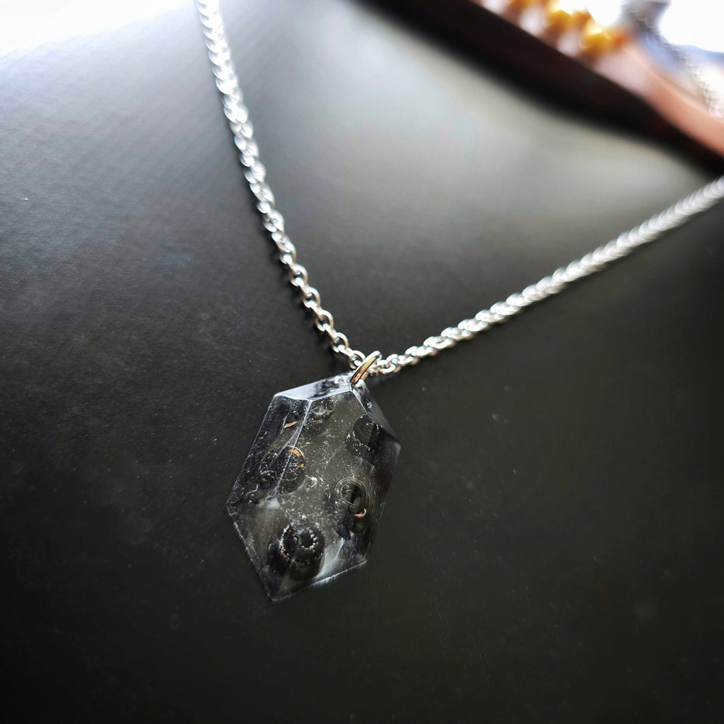 Close-up of Necklace with a resin hexagonal pendant with black guitar string ballends on a dark guitar